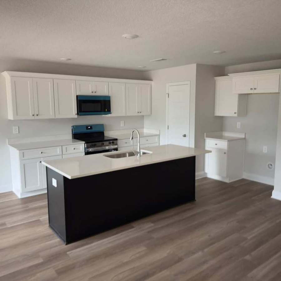 Finished modern kitchen with white cabinets, dark island and luxury vinyl plank flooring